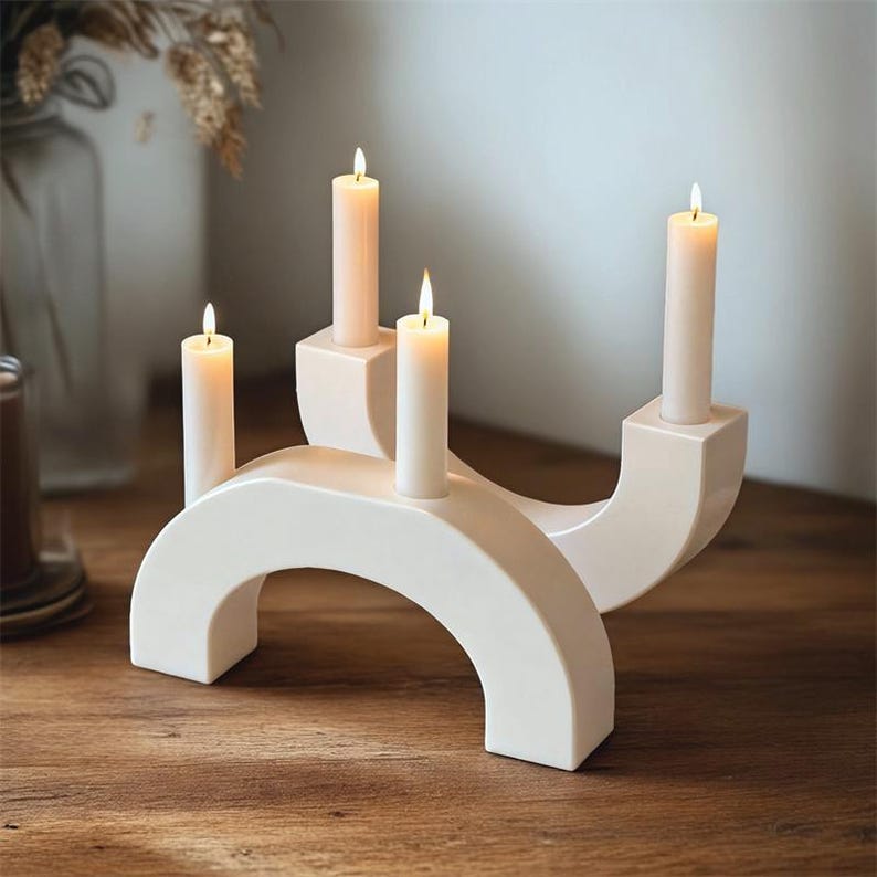 May include: A pair of off-white, arch-shaped candle holders with four lit, cream-colored candles. The candle holders are made of a smooth, solid material and sit on a wooden surface. The candles have a soft, warm glow.