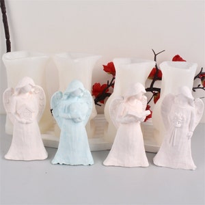 May include: Four white angel figurines with different poses and details. The angels are holding a book, a heart, a birdhouse, and a bouquet of flowers. The figurines are made of a smooth, white material and have a delicate, angelic appearance.