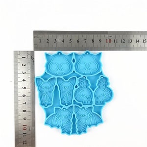 Puede incluir: Molde de silicona azul con ocho formas de tem&aacute;tica de Halloween: dos murci&eacute;lagos, dos calaveras con huesos cruzados, dos murci&eacute;lagos con las alas plegadas y dos calaveras con flores. El molde est&aacute; sobre una superficie blanca con una regla para la escala.