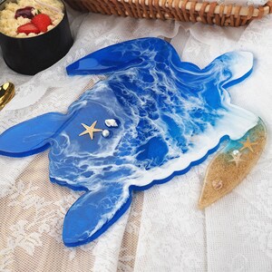 May include: A blue resin turtle tray with white and blue waves, a sandy beach section, and seashells.