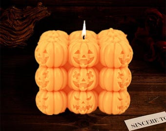 Könnte beinhalten: Eine große orangefarbene Kerze in Form eines Stapels Jack-o'-Lantern-Kürbisse. Die Kerze ist angezündet und hat eine Flamme.