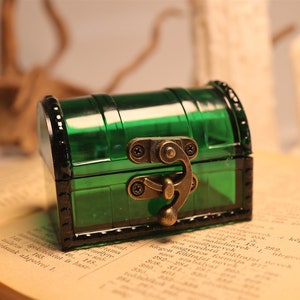 May include: A small, green, plastic treasure chest with a brass latch and hinges. The chest is sitting on top of an open book.