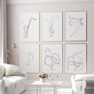 May include: Six black and white line art prints of musical instruments and notes. The prints are framed in gold and hung on a light pink wall.