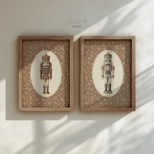 May include: Two framed prints featuring nutcracker figures. Each print has a brown wooden frame and a background with a repeating leaf pattern. The nutcrackers are in oval frames, one in brown tones and the other in white and gold.