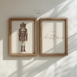 May include: Two framed prints. The left print features a detailed illustration of a nutcracker soldier in brown and tan tones. The right print has the words "MERRY Christmas" in elegant script. Both prints are in wooden frames.