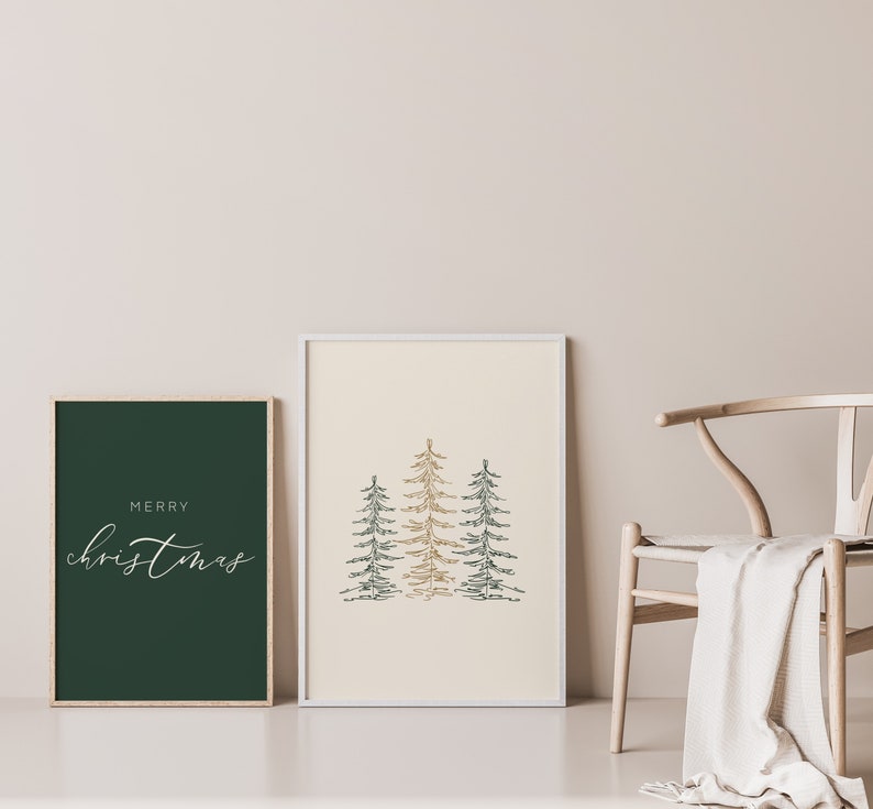 Puede incluir: Dos impresiones enmarcadas, una con el texto "Merry Christmas" en escritura blanca sobre un fondo verde oscuro, y la otra con un dibujo estilizado de tres &aacute;rboles verdes y dorados sobre un fondo crema.