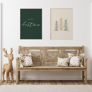 Puede incluir: Un banco de madera con dos cojines que presentan un dise&ntilde;o de corona navide&ntilde;a y un dise&ntilde;o de copo de nieve blanco. El banco est&aacute; contra una pared blanca con dos impresiones enmarcadas, una con el texto "Feliz Navidad" y la otra con una imagen estilizada de tres &aacute;rboles de Navidad verdes y dorados. Una figura de reno dorada se encuentra a la izquierda del banco.