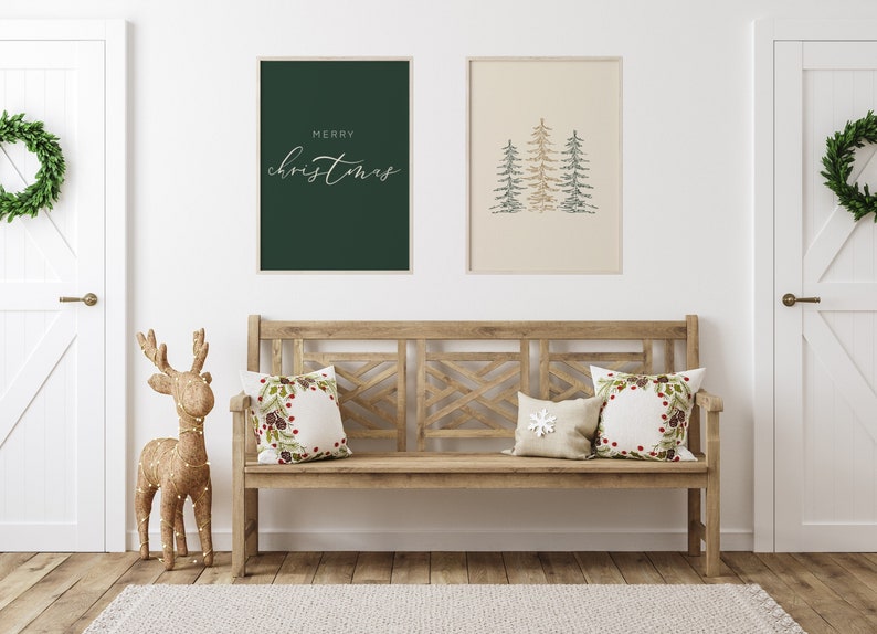 Puede incluir: Un banco de madera con dos cojines que presentan un dise&ntilde;o de corona navide&ntilde;a y un dise&ntilde;o de copo de nieve blanco. El banco est&aacute; contra una pared blanca con dos impresiones enmarcadas, una con el texto "Feliz Navidad" y la otra con una imagen estilizada de tres &aacute;rboles de Navidad verdes y dorados. Una figura de reno dorada se encuentra a la izquierda del banco.