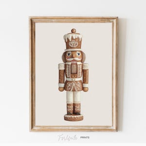 May include: A framed print featuring a detailed illustration of a brown and white nutcracker soldier. The nutcracker has a tall hat, a white mustache, and is wearing a uniform with decorative details. The print is set against a cream background.