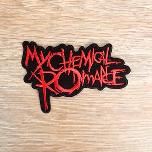 May include: A black embroidered patch featuring the words "MY CHEMICAL ROMANCE" in red, with a distinctive, stylized font. The patch has an irregular outline and is designed to be attached to fabric items.