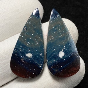 May include: Two teardrop-shaped cabochons of blue, white, and brown opal. The opal has a swirling pattern and white flecks.