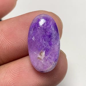 May include: A purple and white oval cabochon gemstone with a cloudy, marbled pattern.