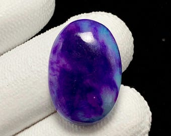 May include: An oval-shaped cabochon gemstone featuring a smooth, polished surface with a vibrant colour gradient transitioning from deep royal purple to bright cyan blue, displaying a glossy finish and a distinct, rounded dome profile.