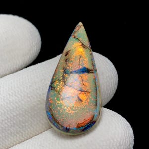 May include: A teardrop-shaped opal gemstone featuring a light base color with vibrant flashes of orange, gold, and blue iridescence. The surface displays a complex network of dark, thin, vein-like inclusions throughout the polished stone.