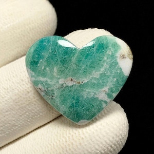 May include: A heart-shaped gemstone featuring a vibrant green color with intricate white veining and small patches of opaque white mineral inclusions throughout the polished surface, showcasing a smooth texture and a glossy, reflective finish.