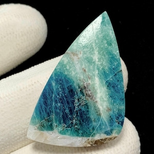 Puede incluir: Una piedra preciosa pulida de forma triangular que presenta un degradado vibrante de tonos azul océano profundo y turquesa brillante. La piedra muestra vetas internas naturales, texturas cristalinas y una superficie lisa y reflectante.