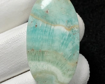 May include: A light blue and white oval cabochon gemstone with a swirling pattern. The stone has a smooth, polished surface.