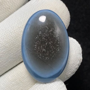 Può includere: Una pietra preziosa ovale a cabochon blu e grigia con un centro bianco e un motivo maculato.