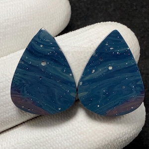 Peut inclure: Deux pierres en forme de goutte d'eau avec un motif tourbillonnant bleu et blanc, rappelant un ciel nocturne. Les pierres polies ont une couleur de base bleu foncé avec des accents blancs et violets. Idéal pour la création de bijoux.