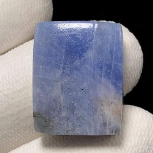 May include: A rectangular, polished gemstone with rounded corners. The stone has a gradient of blue hues, with lighter shades blending into the darker ones. The surface has a subtle, natural texture, and the overall appearance is smooth and refined.