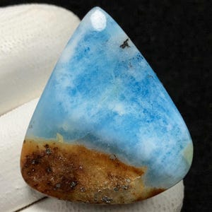 May include: A triangular cabochon of blue and brown celestite with a cloudy, marbled pattern. The stone has a smooth, polished surface.