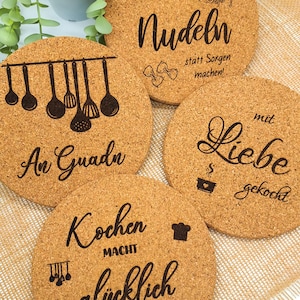 Könnte beinhalten: Vier runde Untersetzer aus Kork mit schwarzem Text und Illustrationen zum Thema Küche. Die Untersetzer zeigen Sätze wie "Kochen macht glücklich" und "Nudeln statt Sorgen machen!" für die Küchendekoration.