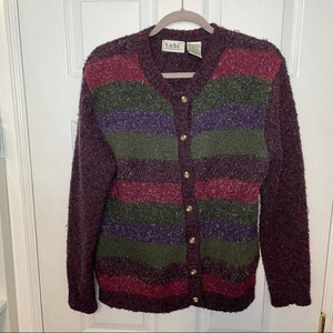Peut inclure: Un cardigan bordeaux à rayures horizontales vertes, violettes et rouges. Le pull à boutons a des boutons dorés et des manches longues. L'étiquette indique "tabi international".