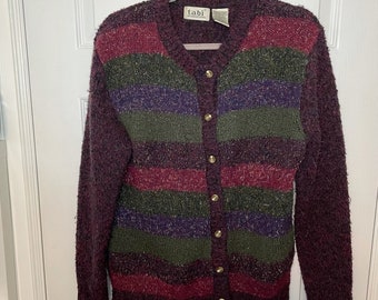 May include: A burgundy cardigan sweater with horizontal stripes in shades of green, purple, and red. The sweater has a button-down front with gold-colored buttons and long sleeves. The label reads "tabi international".