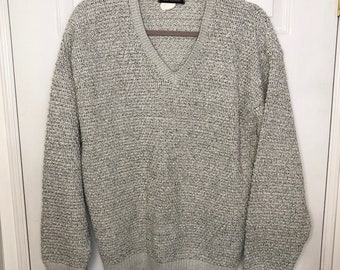 May include: A gray v-neck sweater with a textured knit pattern. The sweater has long sleeves and a ribbed hem.
