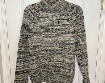 May include: A black and white knit turtleneck sweater with a loose fit. The sweater has a textured knit pattern and a ribbed collar.