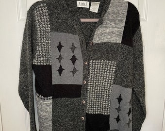 May include: A gray, black, and white patchwork cardigan with a button closure. The cardigan has a star design on the front. The label on the cardigan reads "tabi" and "apparel".
