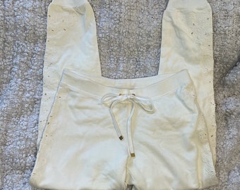 May include: White sweatpants with a lace design on the sides. The sweatpants have a drawstring waist and a relaxed fit.