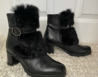 May include: Black leather ankle boots with a faux fur trim around the ankle and a buckle on the side. The boots have a block heel.