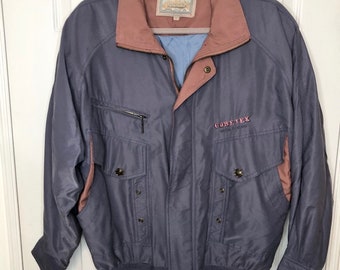 May include: A blue and pink jacket with a zipper closure and a Gore-Tex logo. The jacket has a stand-up collar and two pockets on the front.