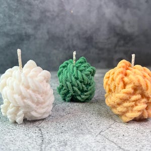 Può includere: Tre candele decorative a forma di corda intrecciata. Le candele sono bianche, verdi e arancioni.