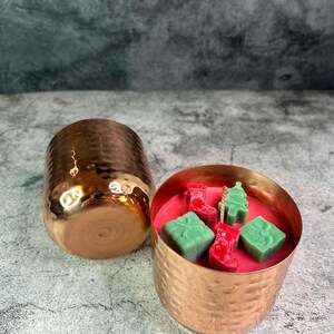 May include: Two hammered copper candle holders, one filled with red wax and green wax melts shaped like Christmas trees, stockings, and presents.
