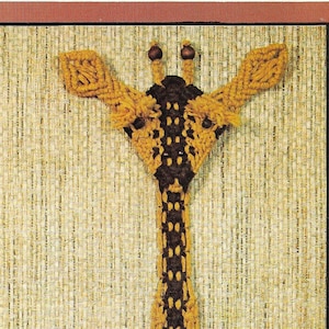 May include: A macrame wall hanging of a giraffe, with a brown and yellow color scheme. The giraffe is hanging on a wall with a green plant in the foreground. The text "Jerome the Giraffe" is printed below the giraffe.