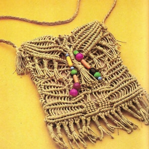 May include: A beige macrame shoulder bag with a woven design and fringe detail. The bag features a long, braided strap and is adorned with colorful beads. The bag is displayed on a yellow background.