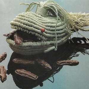 May include: A woven rope basket shaped like a whale with a red bead on the top. The basket is filled with chocolate fish.