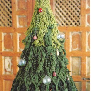 K&ouml;nnte beinhalten: Ein handgefertigter, gr&uuml;ner geh&auml;kelter Weihnachtsbaum mit dekorativen Ornamenten. Der Baum besteht aus verschiedenen Gr&uuml;nt&ouml;nen und hat kleine, bunte Kugeln. Die Basis ist eine Holzscheibe. Der Text unten lautet "More patterns from my shop."