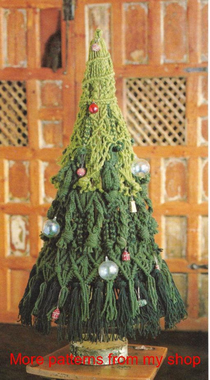 K&ouml;nnte beinhalten: Ein handgefertigter, gr&uuml;ner geh&auml;kelter Weihnachtsbaum mit dekorativen Ornamenten. Der Baum besteht aus verschiedenen Gr&uuml;nt&ouml;nen und hat kleine, bunte Kugeln. Die Basis ist eine Holzscheibe. Der Text unten lautet "More patterns from my shop."