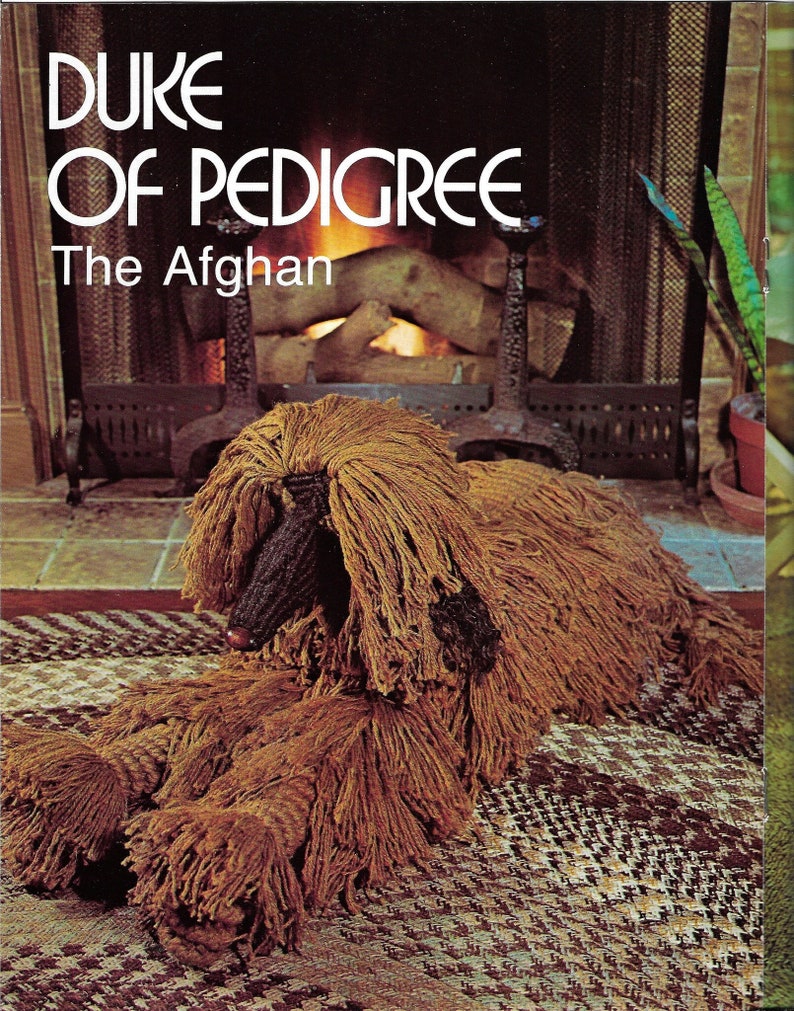 K&ouml;nnte beinhalten: Eine braune Afghanischer Windhund-Skulptur aus Garn, die auf einem gemusterten Teppich vor einem Kamin liegt. Der Text "DUKE OF PEDIGREE The Afghan" ist oben im Bild zu sehen.