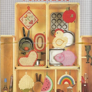May include: Nine crocheted potholders in various shapes and colors, including a heart, a watermelon slice, a rainbow, a chicken, a pig, and a cupcake. The potholders are displayed in wooden crates with numbers 1 through 9.