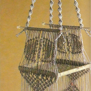 May include: A macrame hanging shelf with three tiers. The shelf is made of natural brown cord and has a woven pattern. The shelf is hanging from four cords that are tied together at the top.