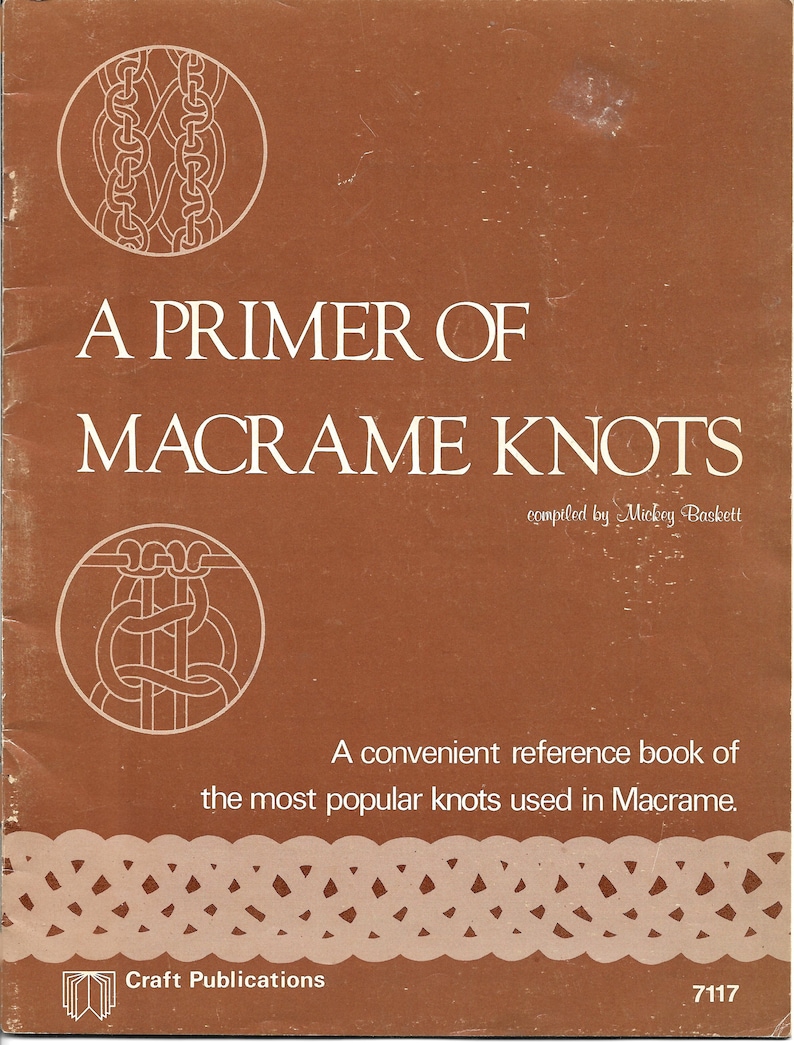 K&ouml;nnte beinhalten: Ein braunes Buch mit dem Titel "A Primer of Macrame Knots" von Mickey Baskett. Das Cover zeigt wei&szlig;e Illustrationen von Knoten und den Text "A convenient reference book of the most popular knots used in Macrame."