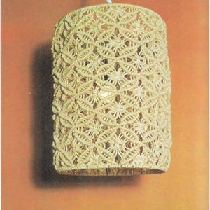 May include: A white macrame lampshade with a geometric pattern hangs from a white cord.