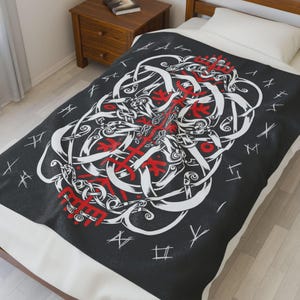 Könnte beinhalten: Schwarze Decke mit einem weißen und roten Wikinger-Design. Das Design zeigt verschlungene Formen und Symbole mit roten Akzenten. Die Decke liegt auf einem Bett mit einem weißen Kissen und einem Nachttisch aus Holz.