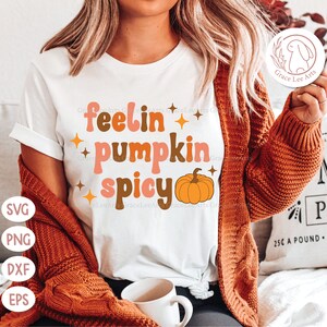 May include: White t-shirt with the text "feelin' pumpkin spicy" in brown, pink, and orange letters. A small orange pumpkin with a green stem is next to the text.