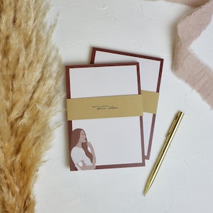 Könnte beinhalten: Zwei braune und weiße Notizblöcke mit einem braunen Papierband, auf dem "wennyschan. your story." steht. Der Notizblock zeigt eine Zeichnung einer Frau mit braunen Haaren und einem weißen Hemd. Ein goldener Stift liegt auf einer weißen Oberfläche.