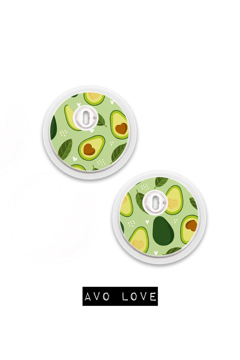May include: Two round, white medical device covers with an avocado pattern on a light green background. The design includes avocado halves, leaves, and small white hearts. The text "AVO LOVE" is displayed in black.